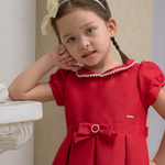 Young girl wearing a red dress with a bow, standing against a neutral background with 'Periwinkle' branding.